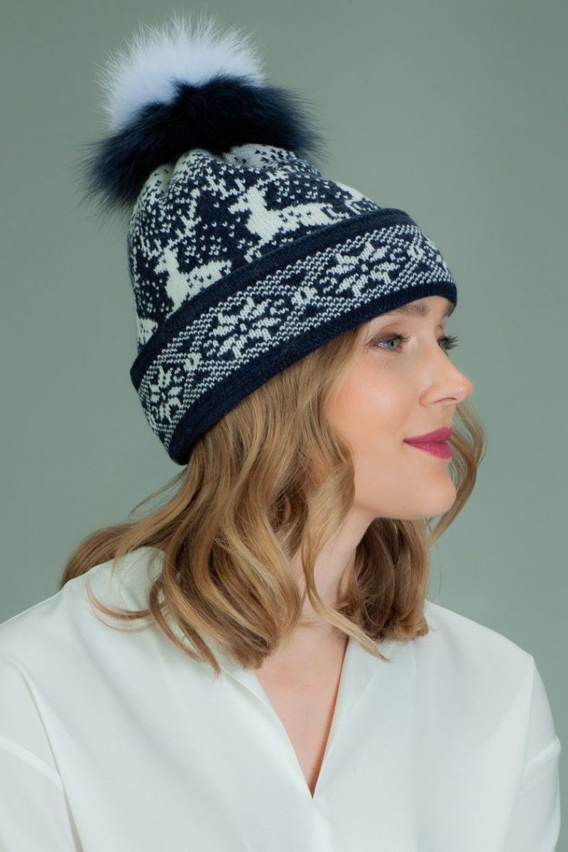 knit wool hat with fur pom pom in white santa deer pattern in dark blue background